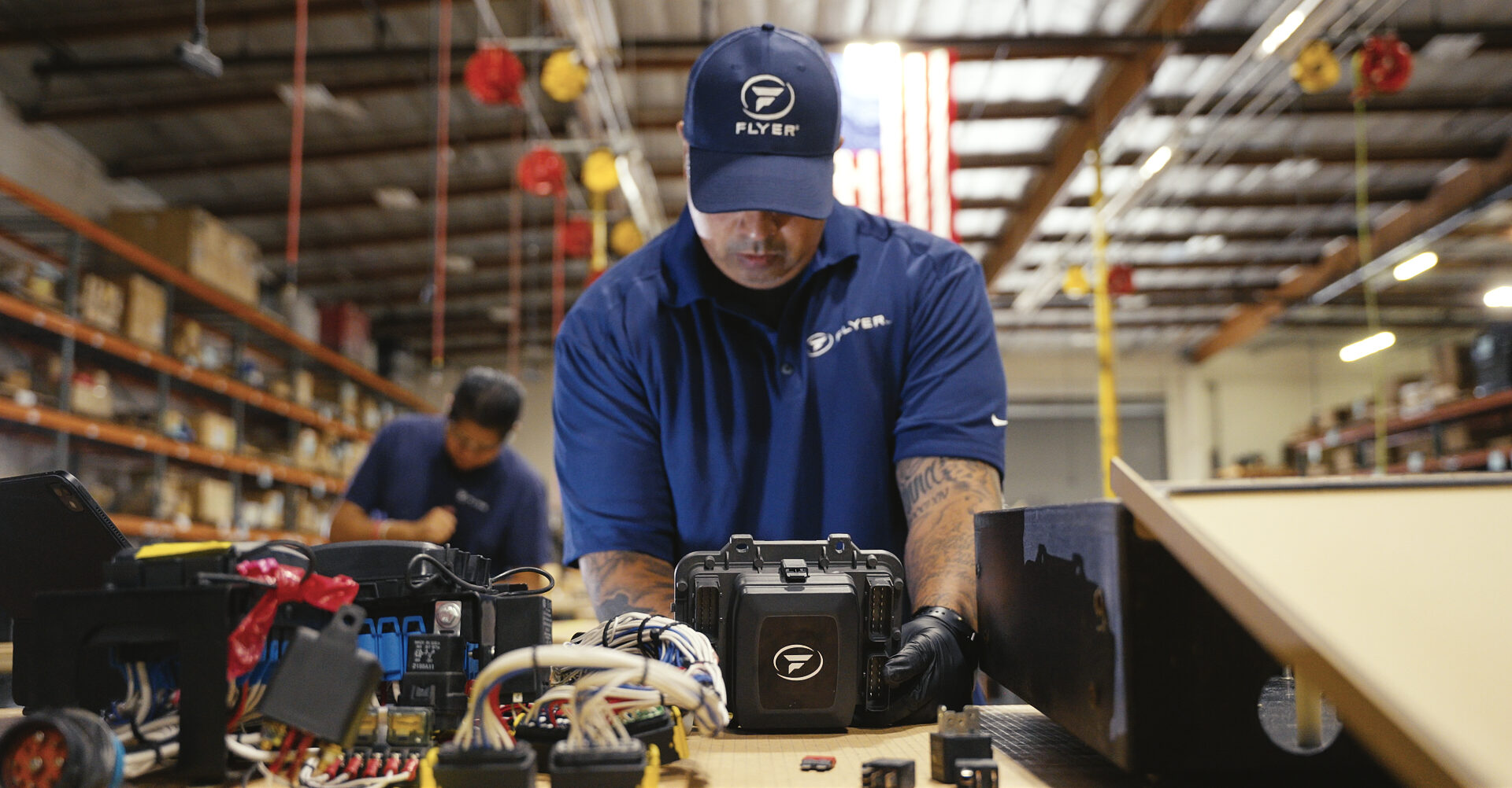 Man from flyer defense holding and working on a vehicle battery in a warehouse - Applied CAx Siemens software