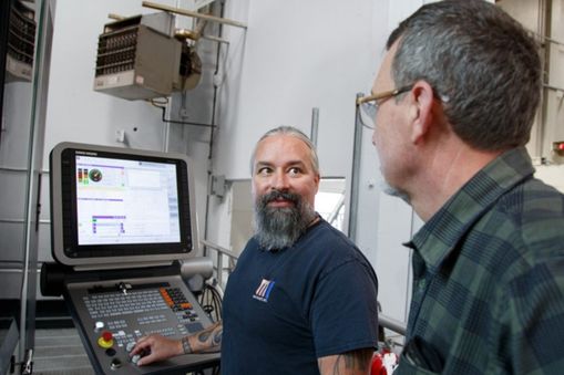 Two men looking at each other with machining software in view - Applied CAx Siemens software