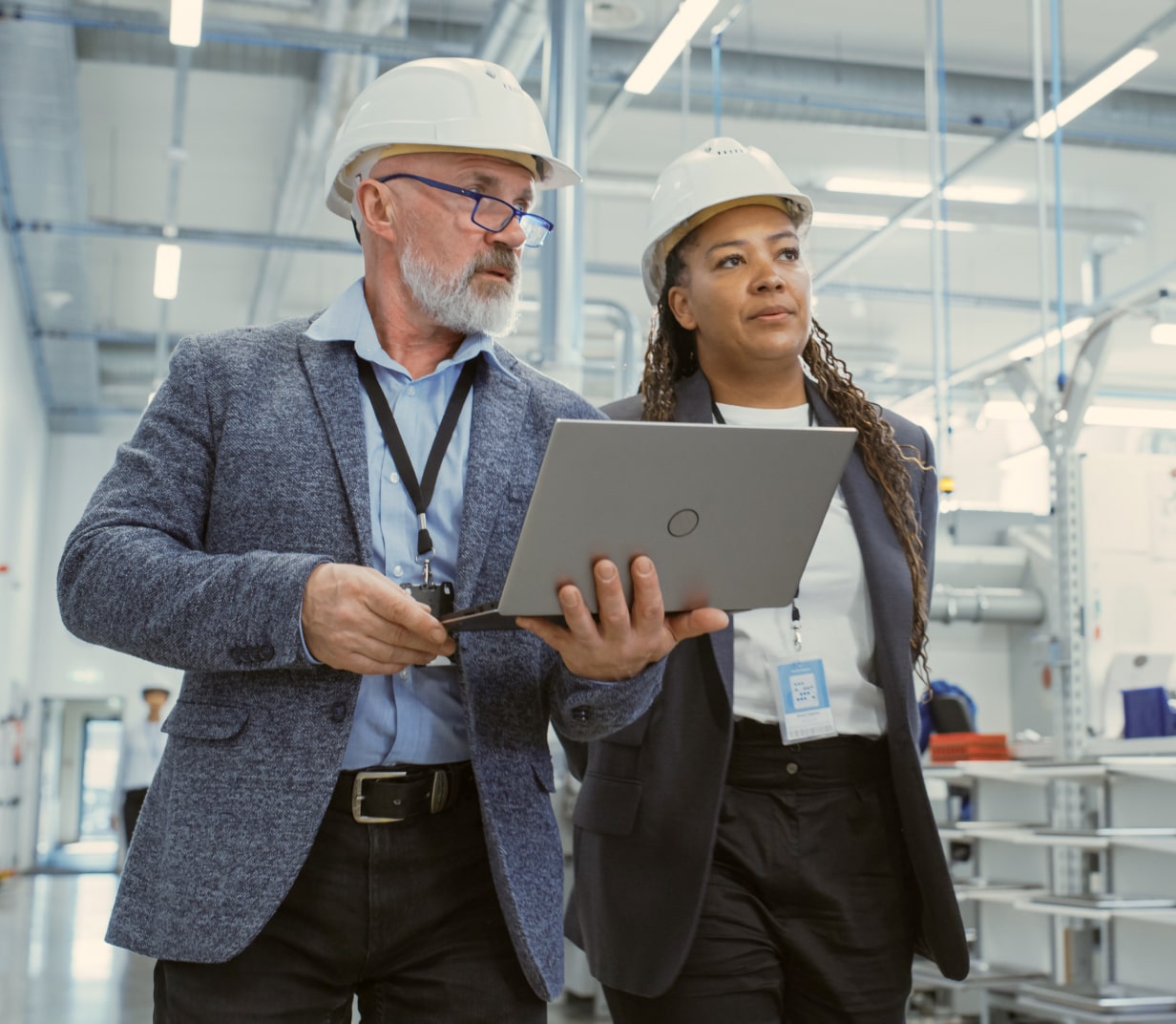 Two people looking at a computer walking through a warehouse - Applied CAx Siemens software